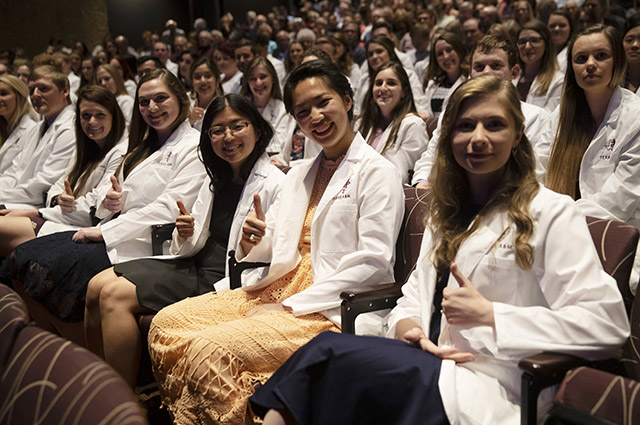 DVM Students at the White Coat Ceremony show the Gig’em thumbs up hand sign while seated